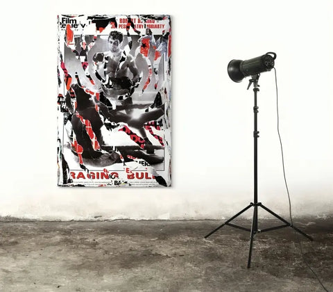 Abstract painting with black, white, and red splatters and text, displayed next to a standing spotlight.