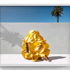 A vibrant yellow, ruffled, petal-like garment worn by a person sitting against a minimalist backdrop.