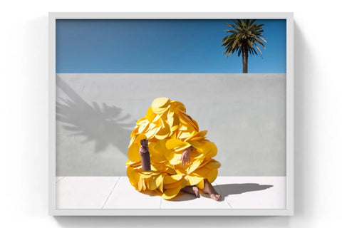 A vibrant yellow, ruffled, petal-like garment worn by a person sitting against a minimalist backdrop.