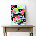 Brightly colored abstract painting on a wooden table in a white room