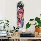 Colorful artistic skateboard deck featuring a portrait painted in vibrant pinks and blues with floral elements.