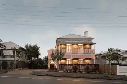 A two-story pink house with a gabled roof, wooden balcony railings, and arched windows.