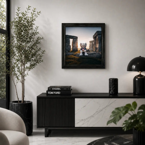 Black-framed original aluminium artwork of a Kaws character sitting among Stonehenge stones at sunset uk Stonehenge Kweam