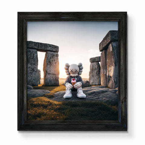 A framed original aluminium artwork of a gray kaws character in a hoodie sitting in front of stonehenge holding ice cream