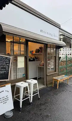 White metal stools with a minimalist design, positioned outside the ’morning kiss’ shop